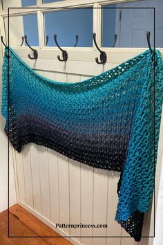 a blue crocheted shawl hanging from a hook on a white wooden wall