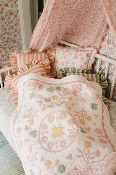 a bed with pink and yellow pillows on top of it next to a wallpapered room