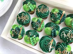 cupcakes with green frosting and gold decorations in a box on a table