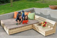 two children are laying on a couch made out of pallet wood and using a laptop