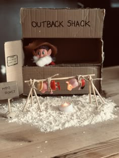 an open cardboard box sitting on top of a wooden table next to a small doll