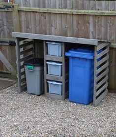 three trash cans are sitting in front of a wooden fence with two bins next to it