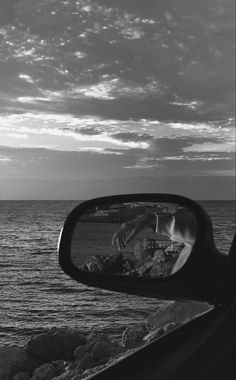 a rear view mirror on the side of a car next to the ocean and rocks