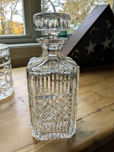 a clear glass bottle sitting on top of a wooden table next to a box and window