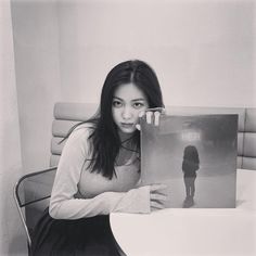 a woman sitting at a table holding up an album with the image of a person on it