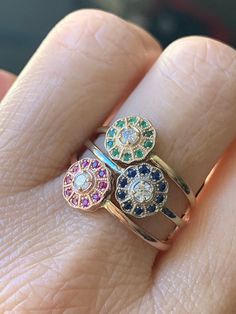 a woman's hand with three rings on it, one has two different colored stones