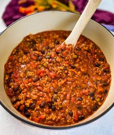 a pot full of chili and beans with a wooden spoon