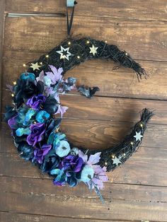 a purple and blue wreath hanging on a wooden wall next to a string light holder