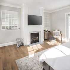 a bedroom with white walls and wood floors, a fireplace in the corner, and a flat screen tv mounted on the wall