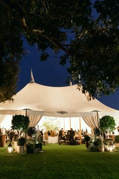 a large white tent is lit up at night with people sitting in it and eating