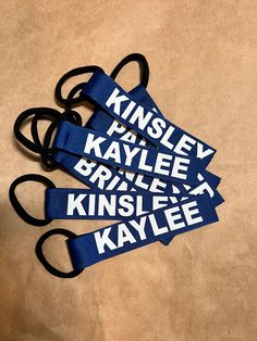 four blue lanyards with white letters on them sitting on a brown surface next to a pair of scissors