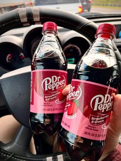 two bottles of soda sitting on top of a steering wheel in front of a car