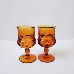 two orange glass goblets sitting next to each other on a white table top