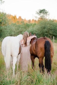 two horses standing next to each other in a field with one woman touching the horse's back