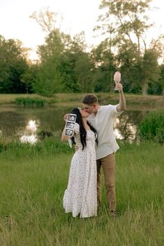 a man and woman are standing in the grass holding an object up to their face