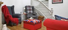 a living room filled with furniture and a stair case next to a red ottoman on top of a hard wood floor