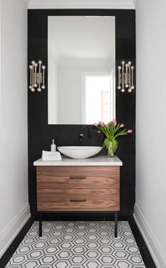 a bathroom with black and white tile, wooden cabinet, sink and mirror on the wall