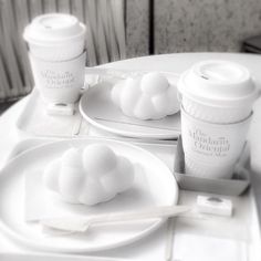 a table topped with white plates and cups filled with liquid next to coffee mugs