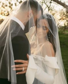 a bride and groom standing under a veil in front of a tree with the sun behind them