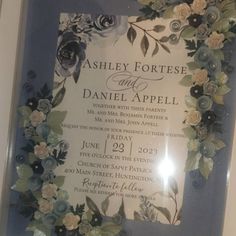 a wedding card with flowers and leaves is displayed in front of a glass frame on the wall