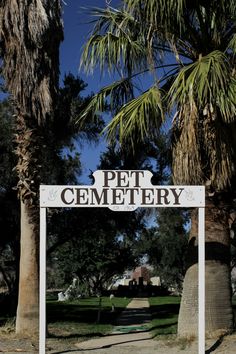 a white sign that reads pet cemetery in front of some palm trees and grass on a sunny day