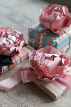 three paper flowers sitting on top of a wooden table next to wrapped gift boxes with ribbons