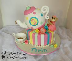 a birthday cake with a teapot and teddy bear sitting on top of the cake