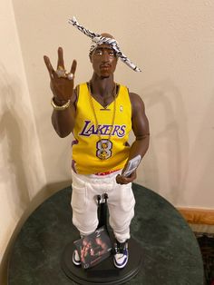 a statue of a man wearing a lakers jersey and holding up his hand with the peace sign