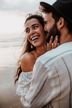 a man and woman standing next to each other on the beach smiling at each other