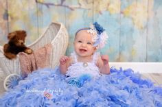 a baby in a blue dress sitting next to a teddy bear