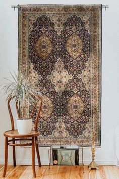 a large rug hanging on the wall next to a wooden chair and potted plant