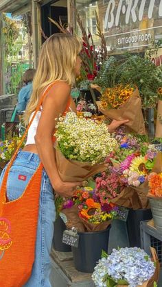 a woman standing in front of a flower shop with lots of colorful flowers on display