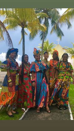 some women in colorful dresses standing next to each other on the grass and palm trees