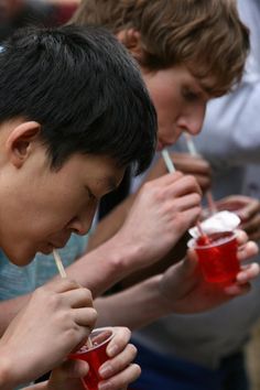 two young men are drinking beverages from plastic cups with straws in their mouths while another man looks on