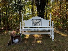 a white bench sitting in the middle of a forest next to a box filled with flowers