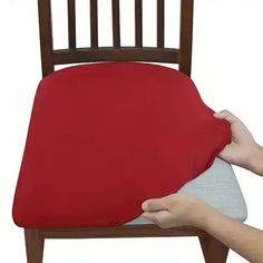 a person holding a red pillow on top of a wooden chair