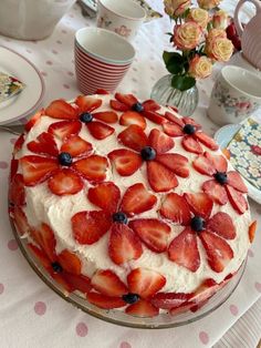 a cake with strawberries on it sitting on a table next to plates and cups