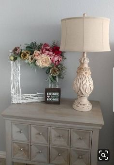 a white dresser with flowers and a lamp on top