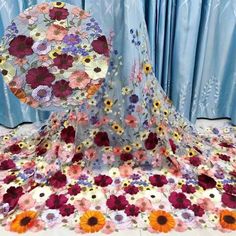 a table topped with lots of colorful flowers on top of a white floor next to a blue curtain