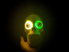 a skull with glowing eyes is shown in the dark while holding it's head