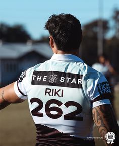 a rugby player with tattoos on his arm and back, looking at the ground while wearing a jersey that reads the star riki