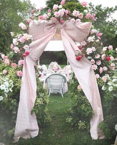 an outdoor wedding ceremony set up with pink and white flowers on the arch, chairs and table