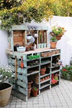 an outdoor garden area with potted plants and pots on the shelf, in front of a white fence