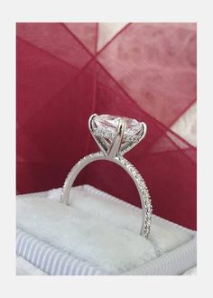 a diamond ring sitting on top of a white box in front of a red background