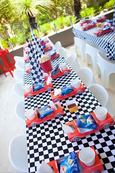 a long table set up with black and white checkered tables cloths, red chairs, and cups