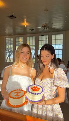 two young women standing next to each other holding cakes in front of the camera and smiling