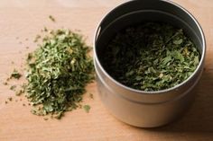 a metal bucket filled with green herbs on top of a wooden table