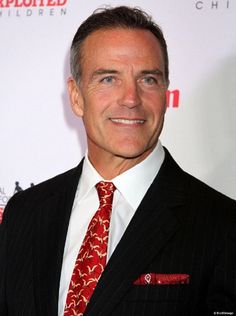 a man in a suit and tie smiles for the camera while standing on a red carpet