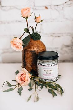 a jar of wildflower candles next to some pink roses on a white counter top