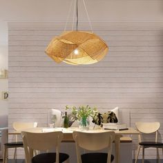 a dining room table with chairs and a light hanging from the ceiling over it, in front of a white brick wall